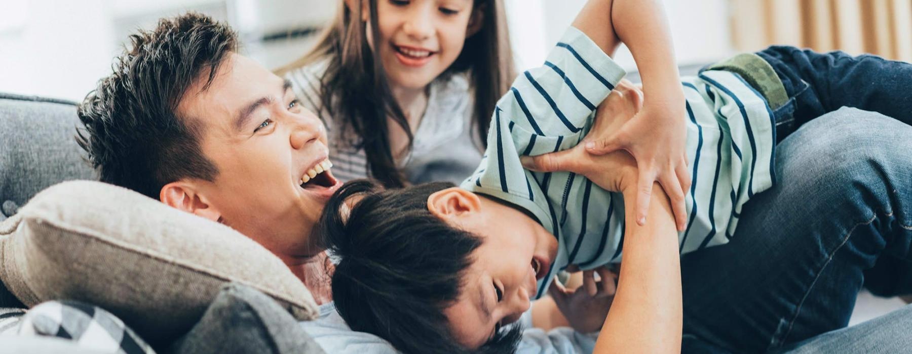 father plays on a couch with his young children