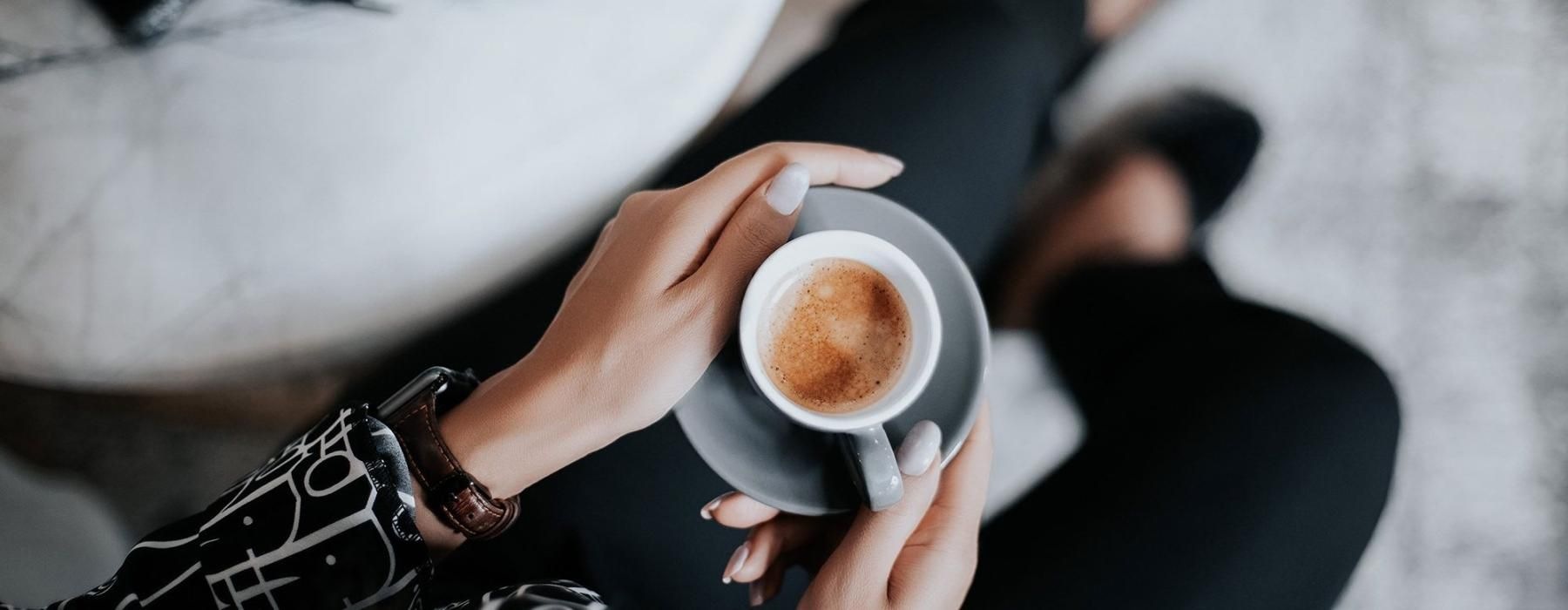 business woman sits next to a marble table with books and holds a saucer with a cup of espresso